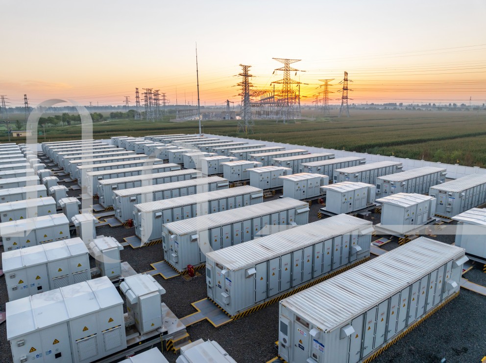 Batteriespeicherpark mit weißen Containern und Strommasten im Hintergrund bei Sonnenuntergang.
